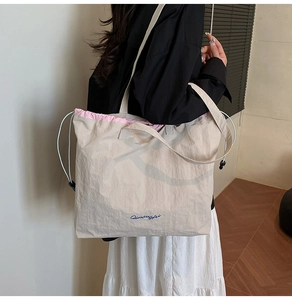 Detail of canvas tote bag with pink drawstring and blue embroidery in a lifestyle setting