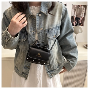 Détail d'un mini sac bandoulière avec nœud en cuir et logo doré sur veste en jean