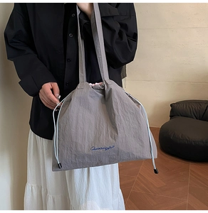 Porté épaule d'un sac cabas gris à cordon avec texture plissée et logo manuscrit bleu