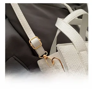 Détail d'un sac en cuir litchi blanc montrant la boucle dorée et le fermoir pivotant