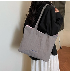 Detail of grey tote bag featuring pink ruffled trim and white drawstring closure