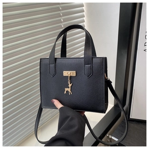 Détail du sac cabas noir avec fermoir doré et pendentif cerf tenu à la main
