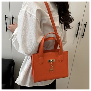 Détail de la texture cuir orange et du pendentif cerf doré sur le sac à main chic