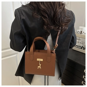 Détail d'un sac à main marron en cuir grainé avec pendentif cerf doré et bandoulière