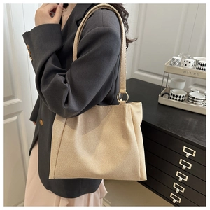 Beige woven canvas tote bag shown worn on shoulder in a cozy indoor lifestyle setting