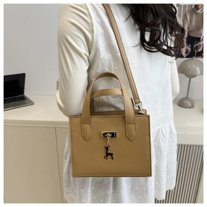 Détail du sac bandoulière marron camel avec pendentif cerf dans un bureau moderne