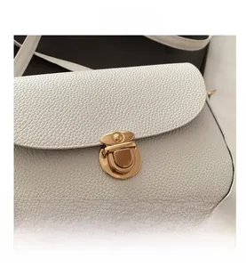 Macro shot of white lychee leather texture and golden metal twist lock on the saddle bag