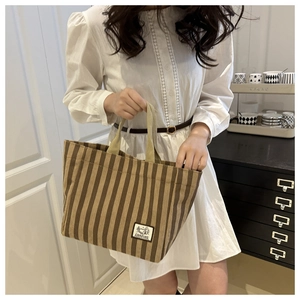 Detail of striped corduroy tote bag with CAMPING label held by model in cozy interior