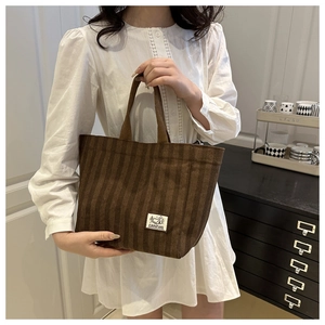 Detail of a brown corduroy tote bag with a Camping patch held by a person in a white dress