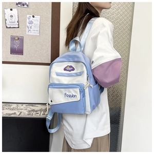 Close-up of blue and white contrast backpack with stylish letter patches shown on a model