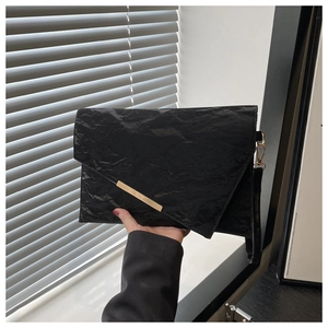 Detail of black envelope clutch featuring unique pleated texture and gold metal bar accent