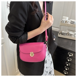Close-up of rose pink saddle bag with litchi texture and gold buckle on black blazer