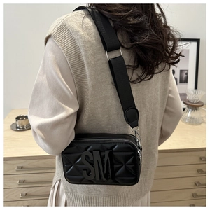 Detail of black quilted camera bag with SM logo and wide adjustable shoulder strap