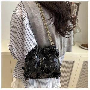 Close-up of black sequined bucket bag with gold chain strap worn by a model