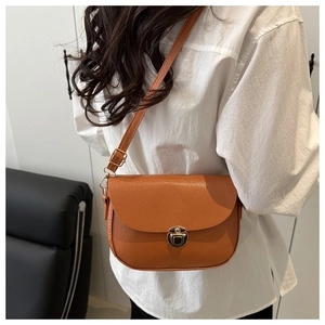 Brown lychee leather saddle bag with golden clasp worn by model in a minimal indoor setting