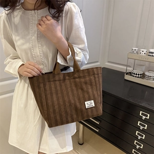 Brown corduroy tote bag with 'CAMPING' label held by model in minimalist interior