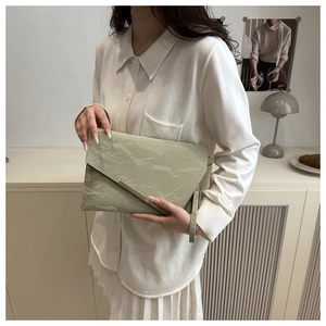 Pochette enveloppe vert sauge avec texture plissée et barre dorée en décor lifestyle