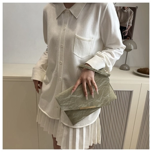 Détail de la pochette texturée vert clair avec bordure dorée et dragonne au poignet