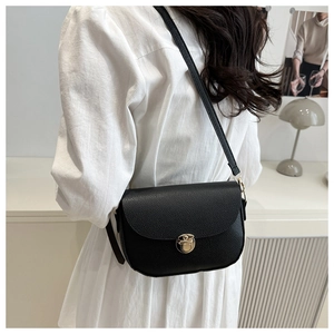 Detail of black pebbled leather saddle bag with gold buckle on a crossbody strap