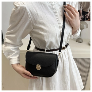 Close-up of black lychee texture saddle bag with metal clasp worn by a model