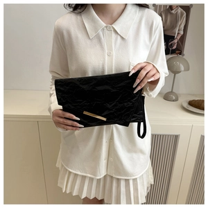 Detail of black pleated envelope clutch featuring a sleek gold metal trim and hand strap