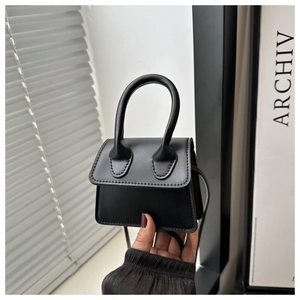 Detailed view of mini black leather handbag held by hand showing micro square bag size