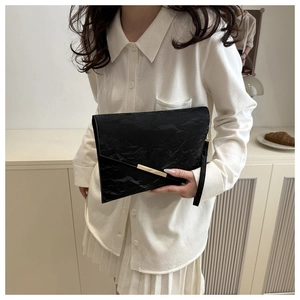 Détail d'une pochette noire avec texture plissée et garniture métallique dorée chic