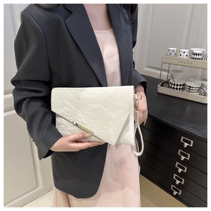 Détail de la pochette crème avec texture plissée unique et garniture en métal doré