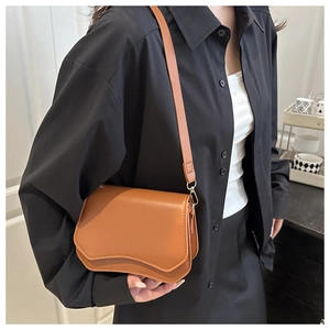 Detail of a brown shoulder bag with a unique wave flap design and gold hardware