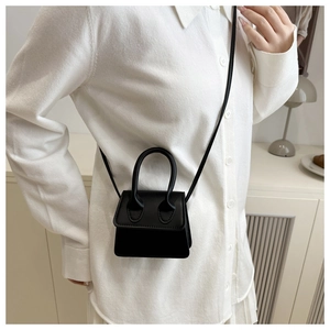 Detail of a black mini trapezoid crossbody bag styled with a white outfit in a soft interior