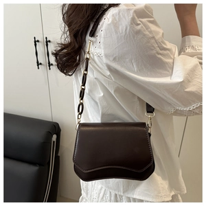 Detail of dark brown shoulder bag with wavy flap design and gold hardware on a model