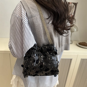 Chic black sequin drawstring bucket bag with gold chain strap shown on a model