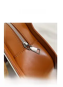 Macro shot of silver metal zipper and precise stitching on brown guitar shaped shoulder bag