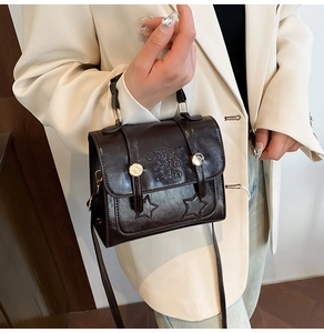Detail of dark brown glossy leather square bag with embossed stars and letters