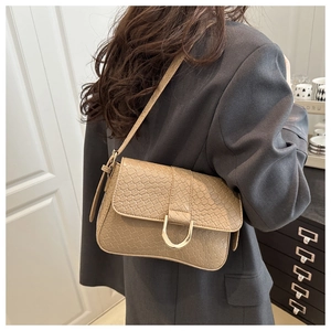 Detail of woven texture beige shoulder bag with gold buckle on a model in gray blazer