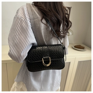 Detail of black woven shoulder bag with golden horseshoe buckle worn on a shoulder