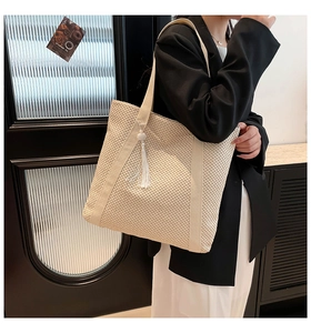 Detailed shot of large beige straw tote bag with white fabric strap and tassel charm