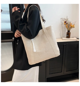 Large straw tote bag with white tassel detail and wide shoulder strap shown on model