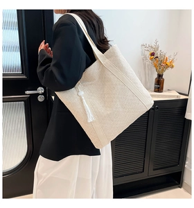Detail of a cream knit tote bag with tassel accent shown on a shoulder in a minimal room