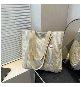 Detail of woven straw tote bag featuring wide fabric straps and a white floral tassel charm
