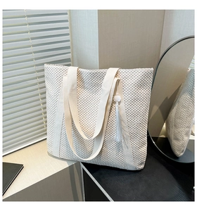 Detail of cream woven tote bag featuring mesh texture, long strap and tassel charm
