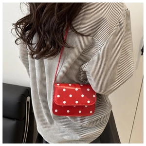Sac à bandoulière rouge à pois porté sur une chemise à rayures et une jupe grise