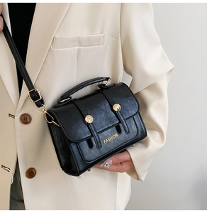 Detail of a black PU leather handbag with a gold metal buckle and fashion logo lettering