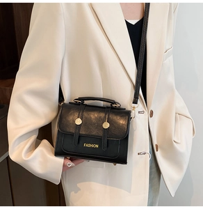 Detail of black pebbled leather crossbody bag with gold Fashion text and metallic buckle