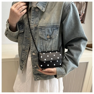 Gros plan d'un mini sac à bandoulière noir et blanc à pois sur une veste en denim