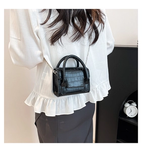 Detailed view of black croc-embossed mini handbag with silver chain strap worn by model