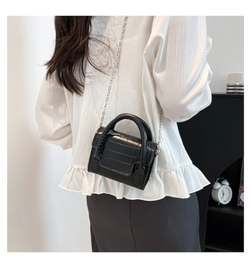 Detailed side view of black croc-effect mini bag with silver chain strap on model