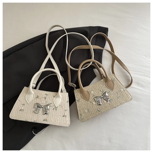 Detailed view of woven straw bag with green floral embroidery and silver bow buckle