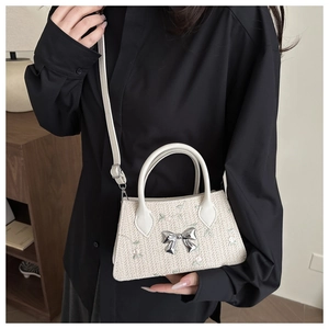 Detail of hand-woven crossbody bag featuring floral embroidery and silver bow ornament