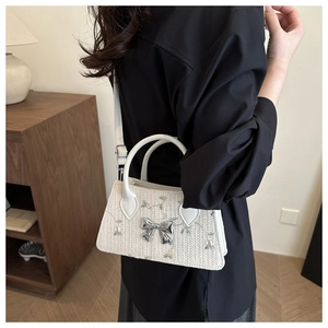 Close-up of white woven straw bag with floral embroidery and silver bow detail